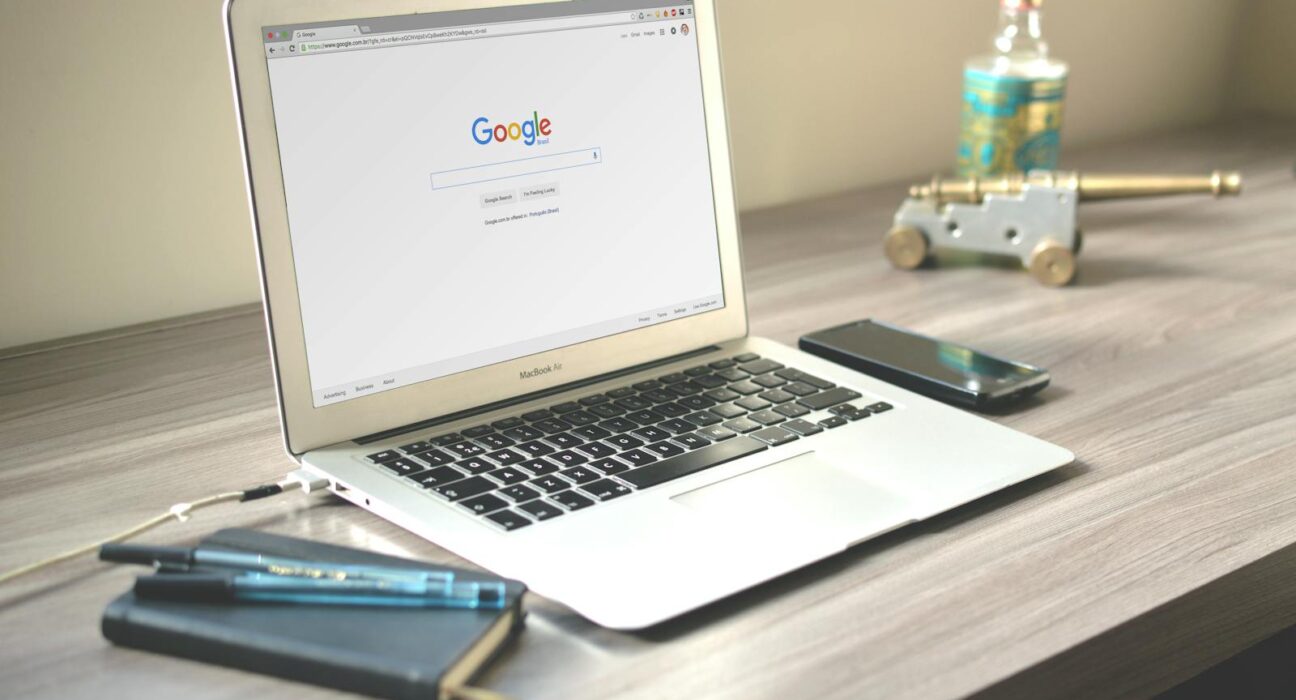 A neat workspace featuring a laptop displaying Google search, a smartphone, and a notebook on a wooden desk.