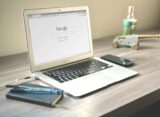 A neat workspace featuring a laptop displaying Google search, a smartphone, and a notebook on a wooden desk.