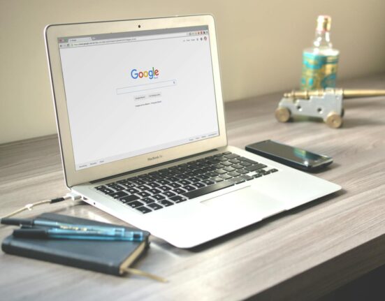 A neat workspace featuring a laptop displaying Google search, a smartphone, and a notebook on a wooden desk.