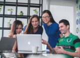 four people watching on white MacBook on top of glass-top table