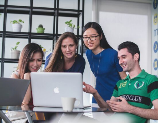 four people watching on white MacBook on top of glass-top table