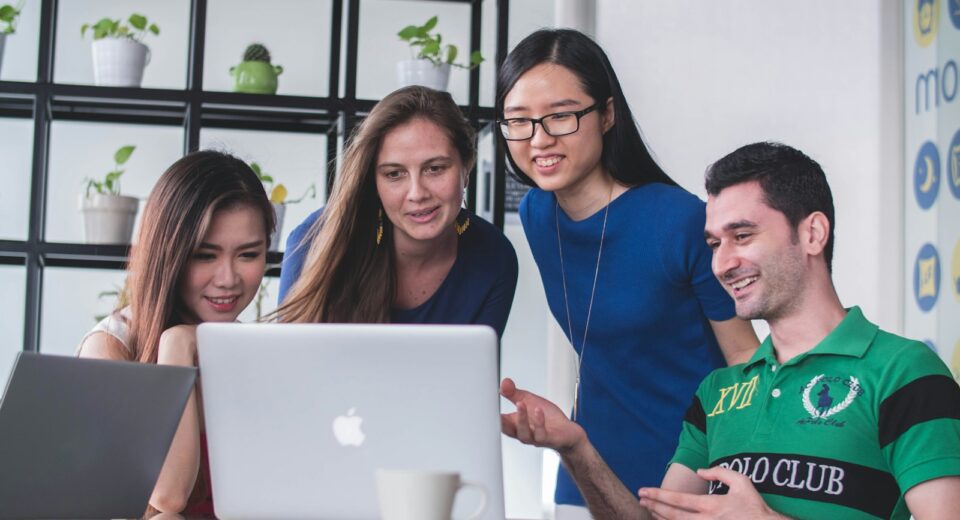 four people watching on white MacBook on top of glass-top table